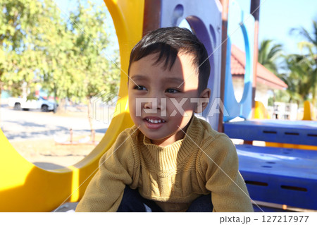 Happy child enjoying outdoor playground activities on a sunny day, wearing a cozy sweater, surrounded by colorful play structures in a joyful environment 127217977