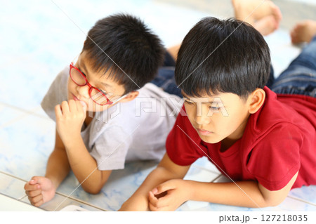 Two Young Boys Engaged in Focused Activity on Soft Floor, One Wearing Glasses and the Other with Short Hair, Bright Colors and Casual Outfits Captured in Natural Light Two Young Boys Engaged in Focused Activity on Soft Floor, One Wearing Glasses and the Other with Short Hair, Bright Colors and Casual Outfits Captured in Natural Light 127218035