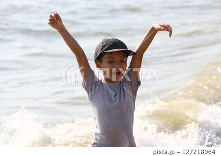 Joyful Child Playing in Shallow Water at the Beach with Hands Raised, Enjoying Nature and Summer Vibes on a Sunny Day by the Shoreline Joyful Child Playing in Shallow Water at the Beach with Hands Raised, Enjoying Nature and Summer Vibes on a Sunny Day by the Shoreline 127218064