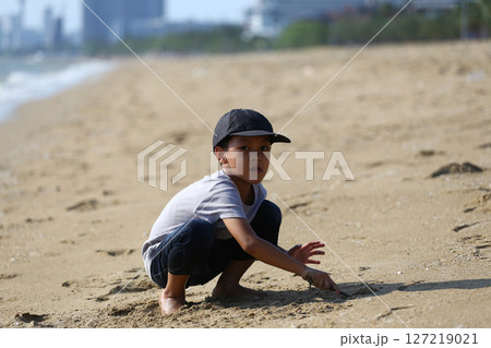 Young child playing in the sand on a sunny beach, enjoying a playful moment, exploring textures, and engaging with nature during a carefree day outdoors. 127219021