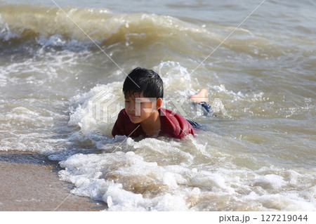 Young Boy Enjoying Playful Moments in Gentle Ocean Waves at the Beach on a Sunny Day, Capturing the Joy of Childhood and Nature's Beauty Young Boy Enjoying Playful Moments in Gentle Ocean Waves at the Beach on a Sunny Day, Capturing the Joy of Childhood and Nature's Beauty 127219044