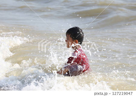 Young child playing joyfully in ocean waves, experiencing the joy of summer at the beach, splashes and water droplets creating a lively and playful atmosphere 127219047