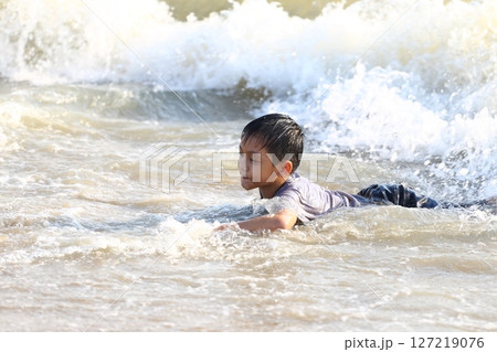 Young boy enjoying a fun day at the beach, swimming in the ocean waves, full of joy and excitement amidst the summer sunshine and splashing water. 127219076