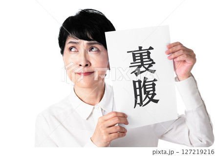 裏腹と書かれた紙を持ち眉間にシワを寄せる中年女性 裏腹と書かれた紙を持ち眉間にシワを寄せる中年女性 127219216
