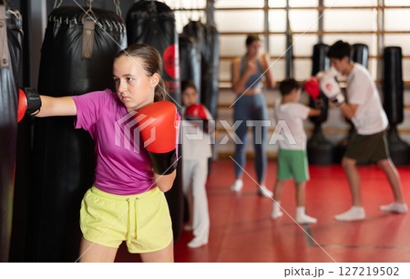 Teen girl in boxing gloves hits punching bag in gym 127219502