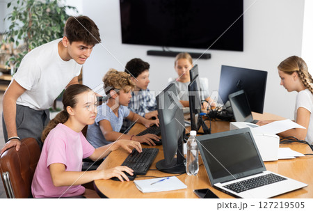 Computer science teacher helps young schoolgirl solve problem on computer 127219505