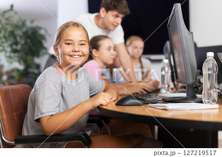 Smiling preteen girl sitting at computer table in training room 127219517