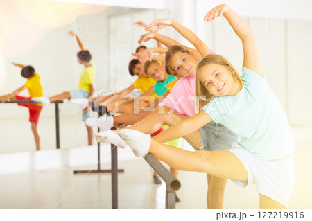Group of children doing leg stretch at ballet barre 127219916
