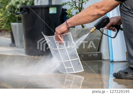 Technician using high pressure water gun for cleaning air conditioner filters. Spraying water on your air conditioner to clear dirt and other debris. Technician using high pressure water gun for cleaning air conditioner filters. Spraying water on your air conditioner to clear dirt and other debris. 127220195