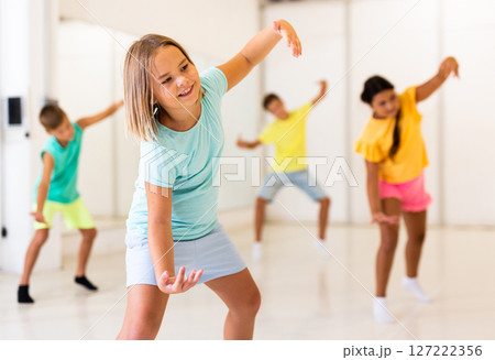 Preteen girl practicing hip-hop movements during group dance lesson 127222356