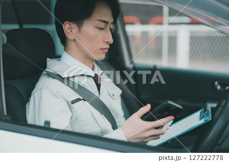 作業着にネクタイ姿の男性の外出先でのスマホ活用 127222778