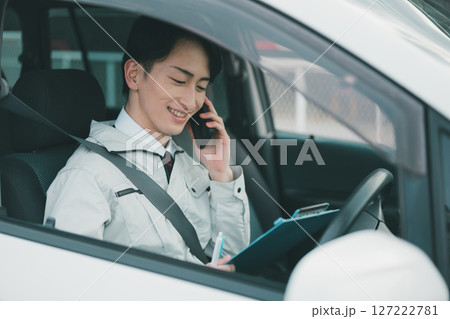 作業着にネクタイ姿の男性が車内で電話をする 127222781