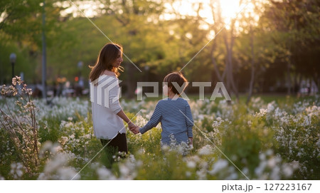 Mother and son enjoy a warm evening stroll through a blooming park filled with wildflowers and golden sunlight Mother and son enjoy a warm evening stroll through a blooming park filled with wildflowers and golden sunlight 127223167