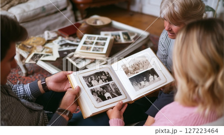 Family members share memories while looking at old photographs in a cozy living room during an afternoon gathering 127223464
