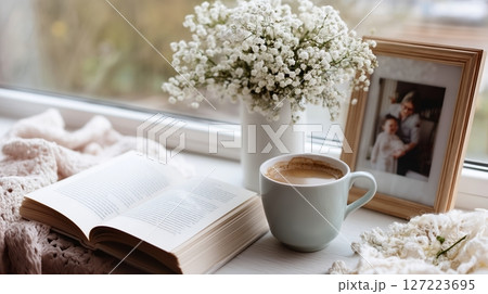 Cozy indoor morning with a book, coffee, flowers, and a family photograph on a window sill Cozy indoor morning with a book, coffee, flowers, and a family photograph on a window sill 127223695