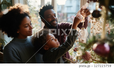 Family decorates Christmas tree together, creating holiday memories in cozy indoor setting during golden hour Family decorates Christmas tree together, creating holiday memories in cozy indoor setting during golden hour 127223759