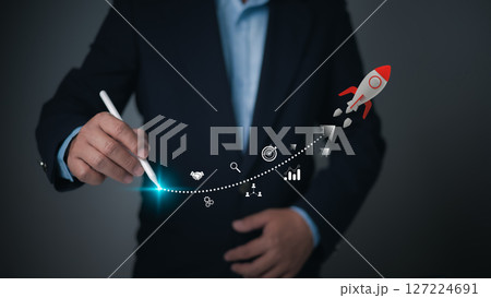 A businessman uses a stylus to chart a vibrant, glowing dotted path for a rocket, symbolizing the trajectory of business growth, strategic planning, and achieving ambitious goals. A businessman uses a stylus to chart a vibrant, glowing dotted path for a rocket, symbolizing the trajectory of business growth, strategic planning, and achieving ambitious goals. 127224691