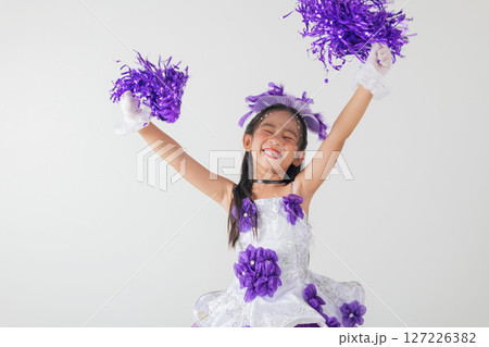 Youthful cheerleader in purple and white outfit holding pom-poms, smiling brightly. Studio image on a clean white backdrop. cheerleader kid Youthful cheerleader in purple and white outfit holding pom-poms, smiling brightly. Studio image on a clean white backdrop. cheerleader kid 127226382