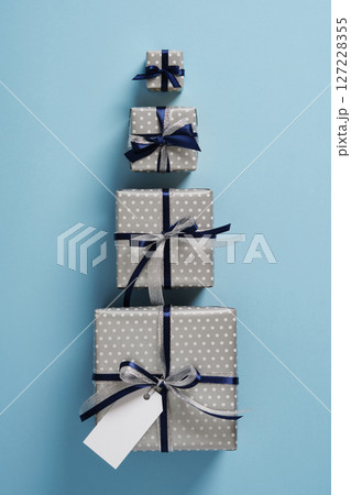 Four gift boxes of different sizes are lined up on a pastel blue background. Each gift is decorated with dark blue and silver satin ribbons. 127228355