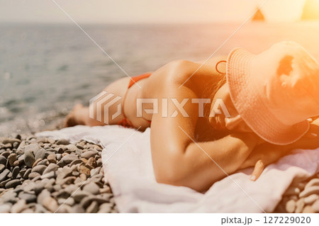 A woman sunbathes on the beach, lying on her stomach in a red swimsuit against the sea backdrop. 127229020