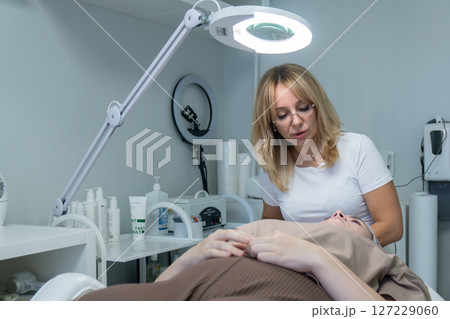 Cosmetology Clinic Facial Treatment Woman Esthetician performs skincare procedure on client during appointment. 127229060