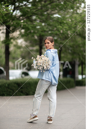 Daisies bouquet woman: Sunny day stroll in park with flowers, wearing casual light blue shirt. Daisies bouquet woman: Sunny day stroll in park with flowers, wearing casual light blue shirt. 127229185