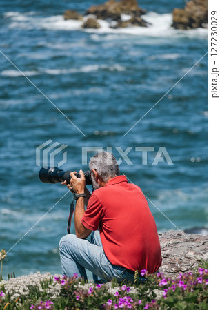Man in jeans and red t-shirt, photographer with camera taking pictures of ocean 127230029