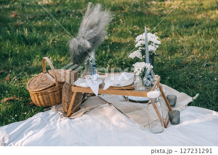Elegant picnic setup on lush green grass with decorative flowers and unique tableware Elegant picnic setup on lush green grass with decorative flowers and unique tableware 127231291