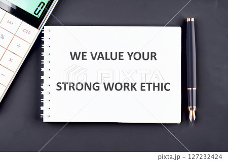 A notepad displaying a motivational message about valuing strong work ethic sits on a desk alongside a calculator and a pen, reflecting a professional workspace 127232424
