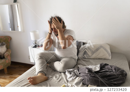 Man suffering from headache sitting on bed holding head in hands 127233420