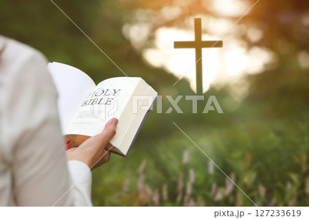 Christian woman holding bible and reading word of God in forest with brightly lit church cross, faith and belief background 127233619