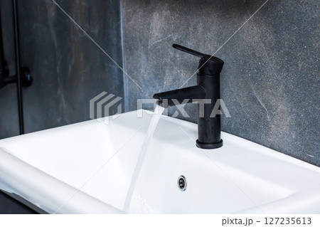 A sleek black faucet is elegantly pouring water into a white sink 127235613