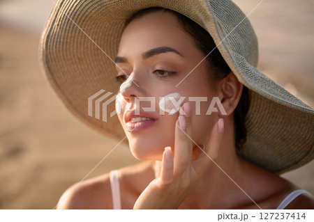 Skincare treatment. Beauty close up portrait of young woman with a healthy skin is applying a facial care product. Cream smear. Sun protection. Girl Uses Sunscreen for Her Skin Skincare treatment. Beauty close up portrait of young woman with a healthy skin is applying a facial care product. Cream smear. Sun protection. Girl Uses Sunscreen for Her Skin 127237414