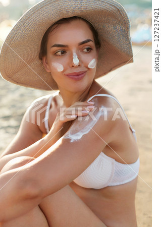 Beautiful Woman in Bikini Applying Sun Cream on Tanned  Shoulder. Sun Protection. Skin and Body Care. Girl Using Sunscreen to Skin. Portrait Of Female Holding Suntan Lotion and Moisturizing Sunblock 127237421