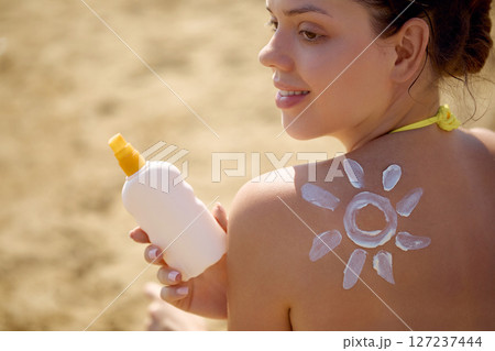 Woman applying sunscreen cream on  tanned  shoulder. Skincare. Body Sun protection suncream. Bikini hat woman applying moisturizing sunscreen lotion on back 127237444