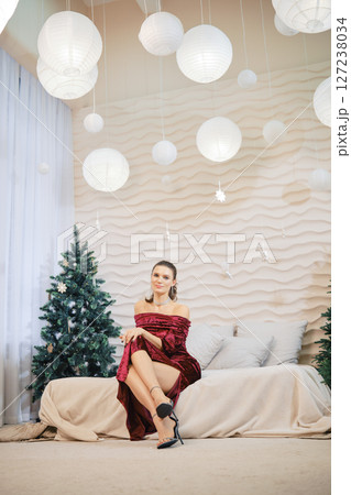 Elegant woman in red dress seated on a sofa surrounded by holiday decorations 127238034
