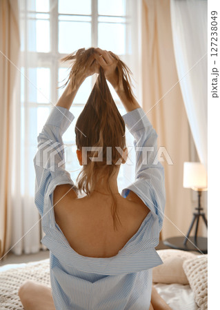 Woman tying hair up in a cozy bedroom with natural light during daylight hours 127238049