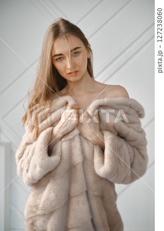 Model poses elegantly in soft fur coat inside modern indoor setting during daylight 127238060