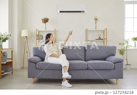 Woman switching on air conditioner at home, blowing warm, cold air room temperature control 127238218