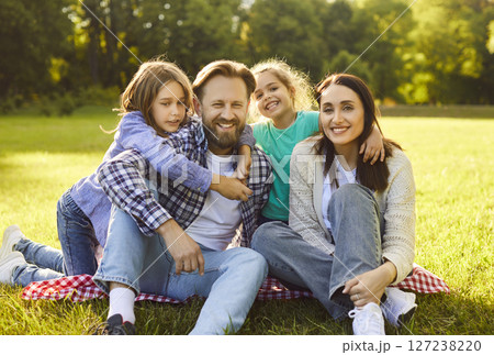 Happy family sitting together on plaid in nature, enjoying picnic time in park, smiling gladfully 127238220