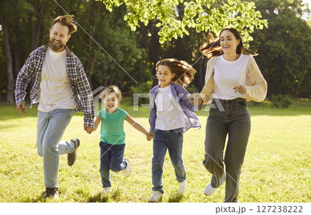 Happy family with two kids running on green grass and having fun in summer park at sunset. 127238222