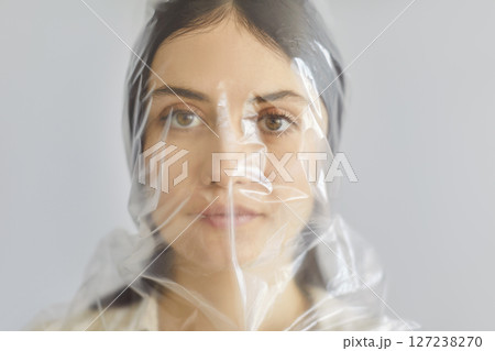 Portrait of beautiful young woman in plastic bag on head looking at camera on gray background. 127238270