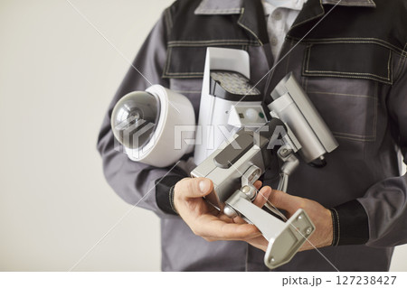 Closeup of male technician holding surveillance CCTV camera in hands on white wall background Closeup of male technician holding surveillance CCTV camera in hands on white wall background 127238427
