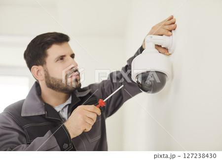 Portrait of young technician man installing surveillance CCTV camera on wall indoors. 127238430