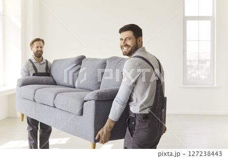 Two happy male movers carrying heavy sofa, transporting furniture during moving day  127238443