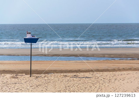 Wooden model of a blue and white boat on pole on a sandy beach, coastal village De Haan, West Flanders, Belgium 127239613