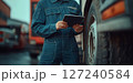 a mechanic in a blue jumpsuit using a tablet while standing next to a truck 127240584