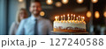 Happy birthday cake with candles in the office, blurred background of smiling male coworkers 127240588