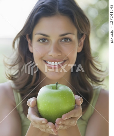 Woman with a radiant smile holding a fresh green apple symbol of health 127241348