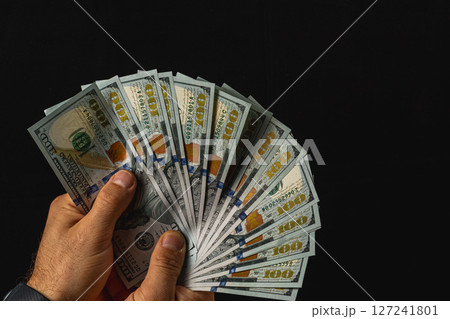 Holding a fan of hundred dollar bills against a dark background 127241801
